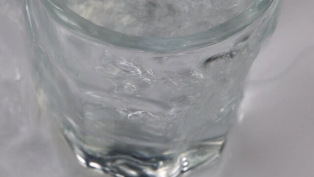 Macro shot of pouring water in a glass and overflowing it with white, clean and clear background. pure clear water.