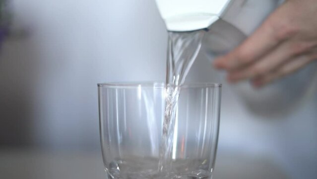Pouring filtered clean clear water into glass cup from carbon based water filter treatment system