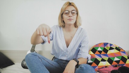 A young woman with glasses is sitting on the sofa, smiling and talking to the camera. Says goodbye...