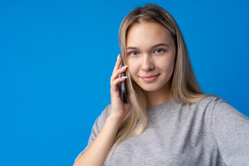 Fototapeta premium Pretty teenage girl talking on the mobile phone against blue background