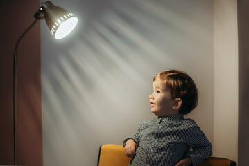 Boy looks at the light from a floor lamp.