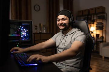 Smiling happy middle-aged man has headset plays computer, learns programming, spends night in front...
