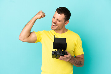 Brazilian man holding a drone remote control over isolated blue background celebrating a victory