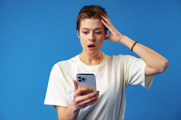 Shocked girl with short hair looking at phone screen with mouth open over blue background