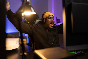 Portrait of relaxed man wearing sweatshirt and cap. The man has won in computer game. He raises hands in the air with joy of victory, triumph along with his virtual team members.