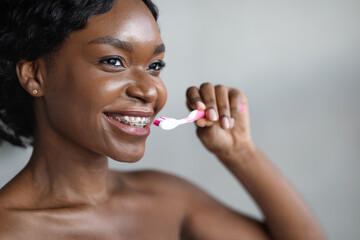 Closeup of young black woman with braces brushing her teeth