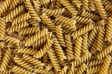 Rotini. Raw fusilli with oats background. Abstract texture of pasta. Pattern of spiral macaroni. Warm food backdrop. Uncooked noodles. Healthy eating and dietary. Soft focus