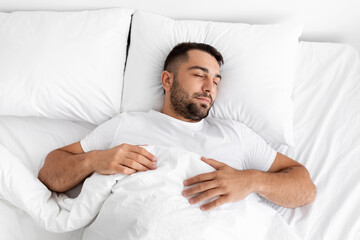Peaceful calm tired millennial caucasian muscular man lies on white comfortable bed, soft pillow,...