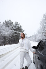 young woman opens the door to the car against the backdrop of a snowy landscape