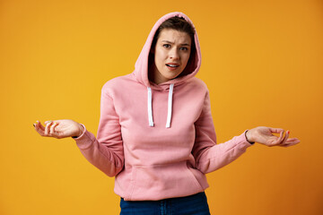 Studio portrait of awkward young woman feeling confused and puzzled shrugs shoulders over yellow...