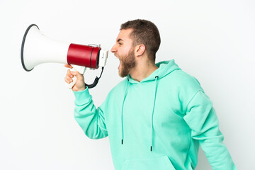 Young handsome caucasian man isolated on white background shouting through a megaphone to announce something in lateral position