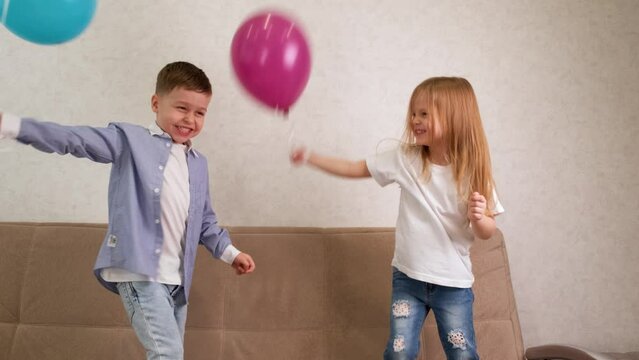 A little girl and a boy are jumping and having fun on the couch with blue and purple balloons. Happy carefree childhood. Children rejoice