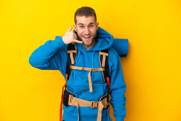 Young caucasian mountaineer man with a big backpack isolated on yellow background making phone gesture. Call me back sign