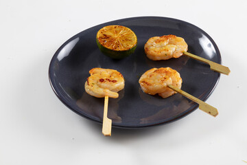 Gambas a la plancha con limón sobre plato de porcelana negro. Grilled prawns with lemon on a black porcelain plate.