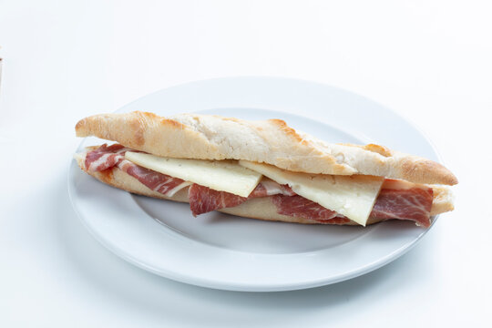 Baguette de jam&oacute;n serrano y queso fresco sobre plato. Serrano ham and fresh cheese baguette on a plate.