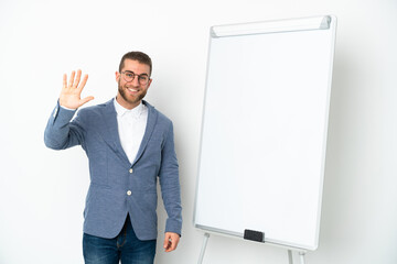 Young business woman giving a presentation on white board isolated on white background saluting with hand with happy expression