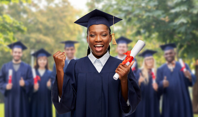 education, graduation and people concept - happy graduate student woman in mortarboard and bachelor gown with diploma celebrating and making winning gesture over group of people on background - obrazy, fototapety, plakaty