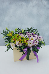 Bouquet of archidea and eustoma in a paper gift box on a gray background. In purple, white and yellow.