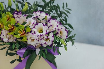 Bouquet of archidea and eustoma in a paper gift box on a gray background. In purple, white and yellow. close up