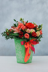 Red bouquet of rose, alstroemeria and eustoma in a green paper gift box on a gray background.