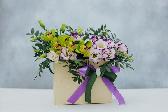 Bouquet of archidea and eustoma in a paper gift box on a gray background. In purple, white and yellow.