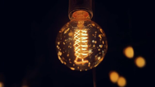 Flickering old fashion tungsten Edison light bulb lamp over black background. Slow motion shot 4K.