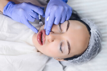 Cosmetologist in beauty salon doing lip augmentation procedure with hyaluronic acid. The beautician...