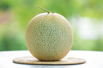 Green Melon on blurred greenery background, Cantaloupe Melon fruit in Bamboo mat on wooden table in garden.