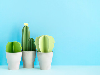 Front view of cute artificial succulent plants in concrete pots on light blue paper background. DIY cartoon paper cactus and succulent border with blank space. Blue wall mockup with green plant .   © shyrokova