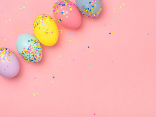 Fototapeta na wymiar Bright coloured and decorated with confetti easter eggs in a row on a pink backdrop. Festive springtime design for greeting card, invitation, holiday banner. Minimalist Easter composition, copy space.