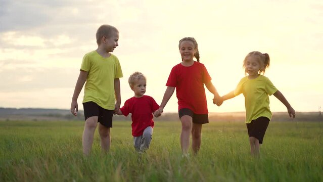 Happy family. Children walk holding hands. Kids play in park on green grass. Children walk in field at sunset. Weekend picnic in nature. Childhood dream concept.Happy family of kids cheerful childhood