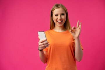 Young smiling woman holding smartphone and showiing OK sign