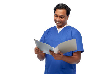 Obraz na płótnie Canvas healthcare, profession and medicine concept - happy smiling indian doctor or male nurse in blue uniform with folder reading medical report over white background