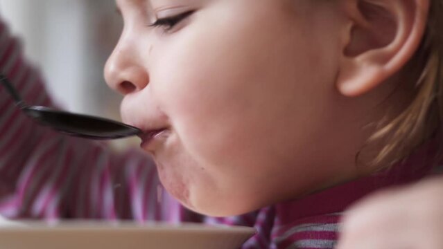 Close up of preschool girl portrait with eating soup at home. picky eater 