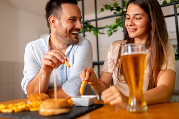 Couple eating burgers and drinking beer at home
