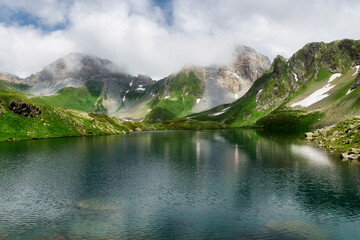 mountain landscape with small glacial lake . Mountain peaks with snow, green grass in the foreground