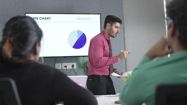 Young Indian businessman corporate angry leader coach speaker give flip chart workshop presentation explaining strategy teaching multi ethnic staff consult diverse team at office meeting training.