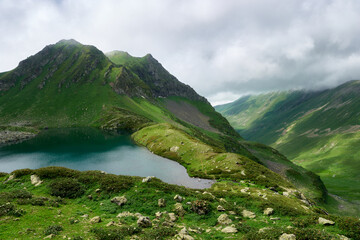 mountain landscape with small glacial lake . Mountain peaks with snow, green grass in the foreground