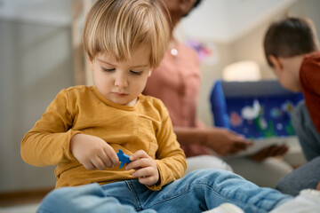 Small boy sits on the floor and plays with toy animal at kindergarten.