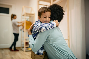 Affectionate Caucasian boy embraces his African American mother while greeting on first day at...