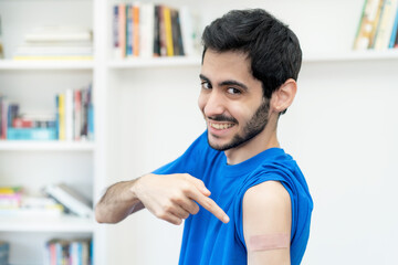 Laughing arabic man showing plaster on arm after third vaccination against Covid 19