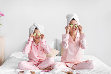 Happy asian teen girl and young woman have fun, apply cucumber slices to eyes, sit on bed with...