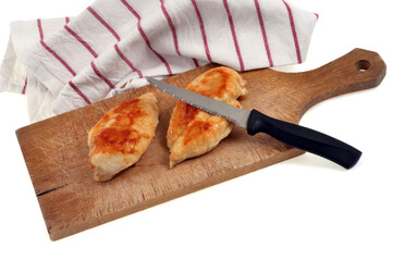 Blancs de poulet cuits sur une planche à découper avec un couteau à côté d'un torchon sur fond blanc