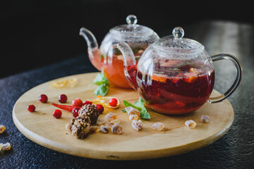 Two teapots with fruit berry tea on a round textured wooden board on a black table in a restaurant....