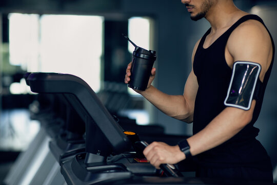 Male Athlete With Sport Shaker And Phone Armband Using Treadmill At Gym