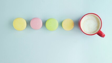 Top view of multicolored French Macarons cookies and a cup of coffee on a pastel blue background