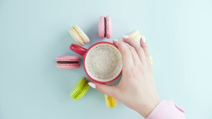 Top view of multicolored French Macarons cookies and a cup of coffee on a pastel blue background