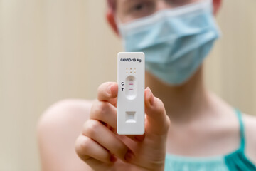 Teenage girl wearing face mask holding Covid-19 rapid antigen test cassette with positive result of rapid diagnostic test