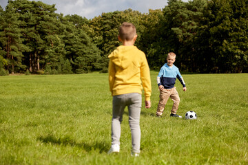 Naklejka premium childhood, leisure games and people concept - happy little boys with ball playing soccer at summer park