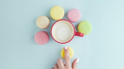 Fototapeta na wymiar Top view of multicolored French Macarons cookies and a cup of coffee on a pastel blue background